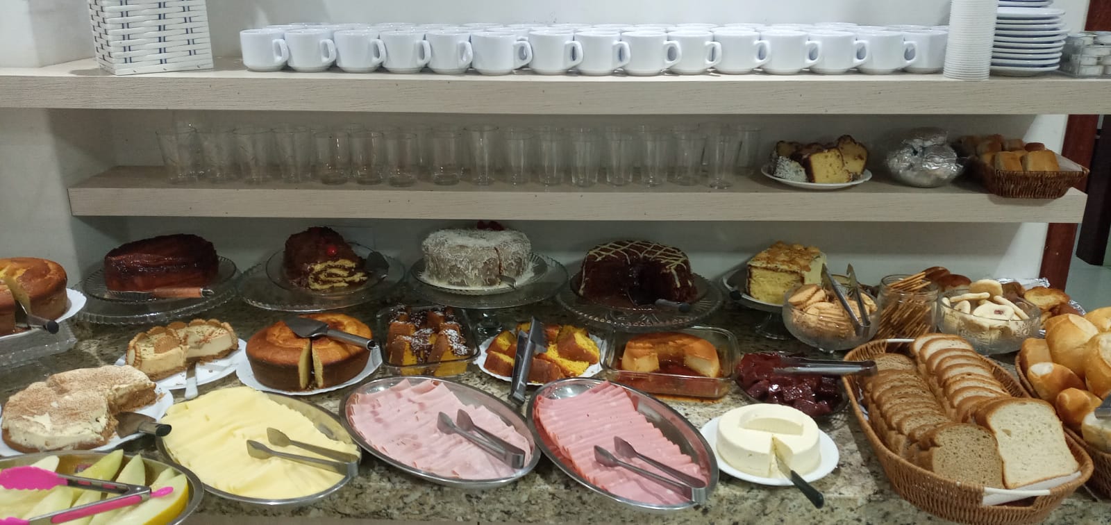 Variedade de bolos, frios, pães e bebidas do café da manhã